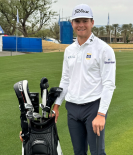 Michael Brennan stands on a golf course next to his Titleist golf bag, holding a golf club.