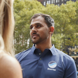 A person in a blue Stavtar polo shirt engages in conversation outdoors.