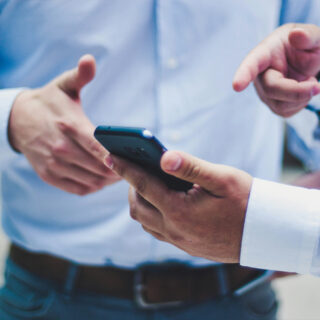 Two people in business attire are engaged in conversation, with one holding a smartphone.