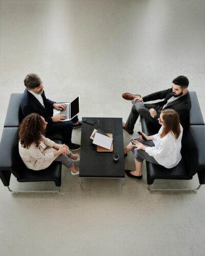 Four people sit around a black coffee table in a modern office setting, engaged in discussion.